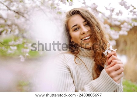 Happy woman enjoying scent in blooming spring garden. The concept of youth, love, fashion, tourism and lifestyle. Royalty-Free Stock Photo #2430805697