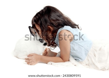 Cute little girl kissing rabbit while lying on floor. Joyful kid with her pet on white background. Happy child playing with her cute bunny. Children gently take care for pets with love.