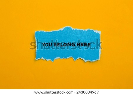 You belong here words written on blue torn paper with orange background. Conceptual business photo. Top view, copy space for text.