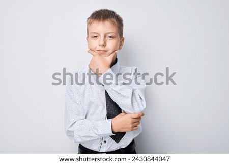 Thoughtful young boy in a shirt and vest posing with hand on chin against a gray background.