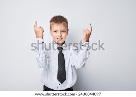 Smiling young boy in shirt and tie pointing upwards against a white background, space for text.