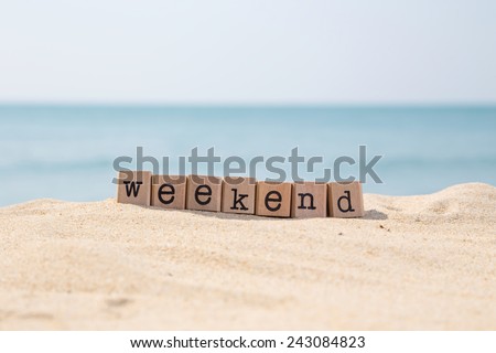 Weekend word on wood rubber stamps stack on the sand beach for vacation and summer season concept, beautiful ocean view during daytime on a sunny day with blue sky on background Royalty-Free Stock Photo #243084823