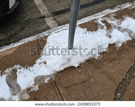 A metal pole along a sidewalk with snow around it.