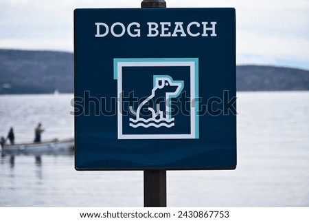 drawing of a dog on a blue sign indicating a dog beach with a fishing boat sailing on the sea in the background.