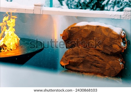 Firewood in bags next to round barbecue in winter