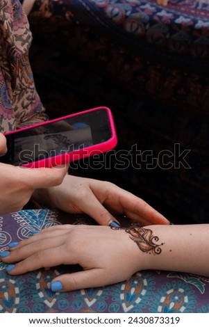 Close-up of a henna tattoo on a hand holding a smartphone, showcasing intricate design against a patterned fabric background