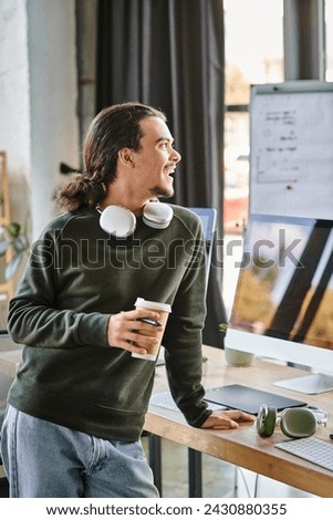 Relaxed young man standing with stylus pen and coffee while laughing in post-production workspace
