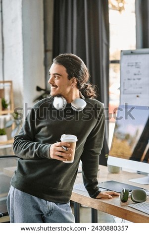 Relaxed young man standing with stylus pen and coffee and smiling in post-production workspace