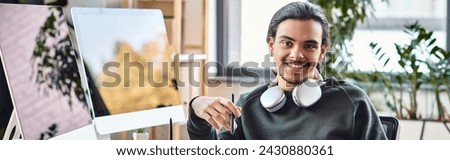 Relaxed young man with stylus pen smiling at a startup post-production workspace, banner