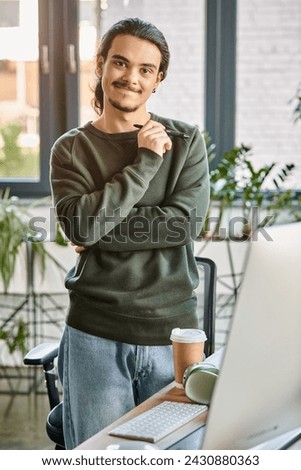 Relaxed professional standing with stylus pen and smiling in post-production workspace, man in 20s