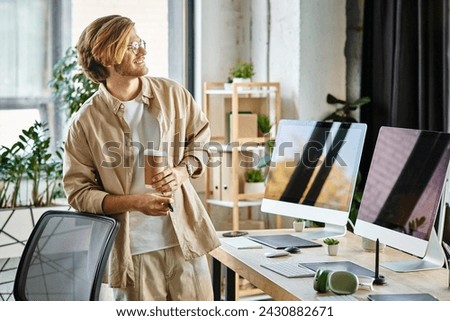 cheerful man in glasses holding coffee and stylus pen in modern office setup, post production