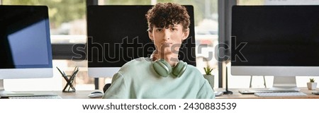 curly haired young man with headphones sitting near computer monitors, post production banner