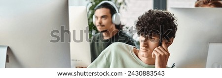 focused curly man engaged in retouching work with stylus pen in hand looking at monitor, banner