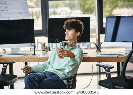 young curly-haired man sitting in office chair and holding coffee to go, post production team member