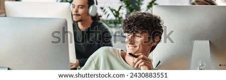 happy curly man engaged in retouching work with stylus pen in hand looking at monitor, banner