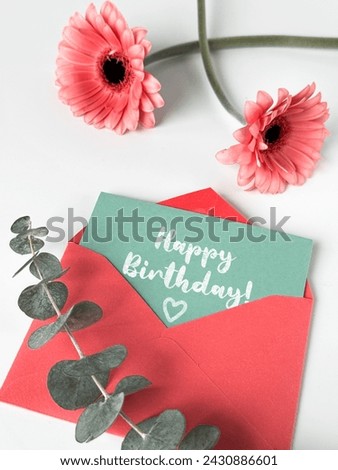 An image of a pink envelope with a vibrant happy birthday card placed on top of it with pink gerbera flowers.
