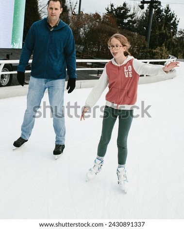 Daughter and father ice skate together on path on skates