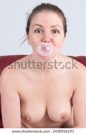 A topless blonde woman blowing a bubble