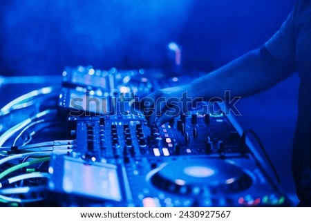 Close up of dj hand making music with mixing console on an electro music festival. Cropped picture of a hand with mixing console at night with blue neon light.
