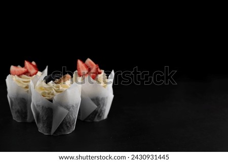 On a dark background, cupcakes with cream, decorated with strawberries and blueberries.Background for writing text.