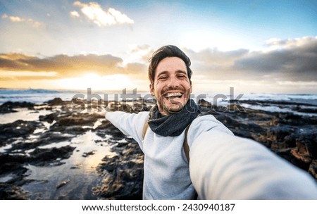 Handsome young man taking selfie pic with smart mobile phone outdoors - Traveler guy smiling at camera with sunset on background - Traveling life style and technology concept 