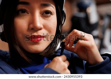Detailed view of woman dressed in winter clothing grasping and adjusting snow helmet on her head. Close up shot of asian female guest securing headgear preparing for skiing and snowboarding adventures Royalty-Free Stock Photo #2430955393
