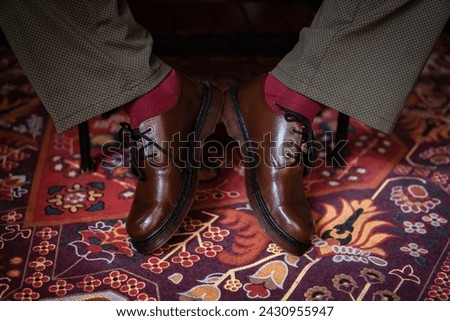 Close-up of a concept photo of 3-hole boots made of genuine leather worn indoors on a classic red carpet. Pira feet in stylish brown boots on the Turkish red carpet