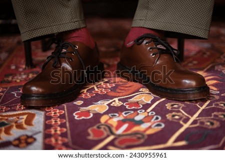 Close-up of a concept photo of 3-hole boots made of genuine leather worn indoors on a classic red carpet. Pira feet in stylish brown boots on the Turkish red carpet
