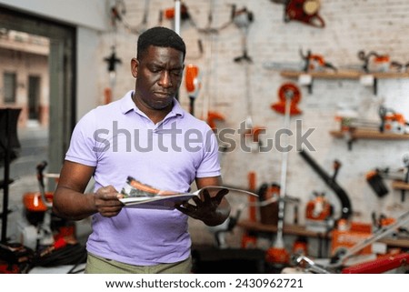 African-american man reading price catalogue while standing in salesroom of gardening tools store. Royalty-Free Stock Photo #2430962721
