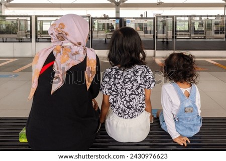 A Muslim mother with her two daughters sitting on the bench at Jakarta MRT train station. Waiting for the train to arrive.