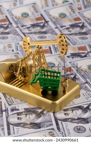 Gold miniature oil pump and shopping cart with 100 US dollar bills background