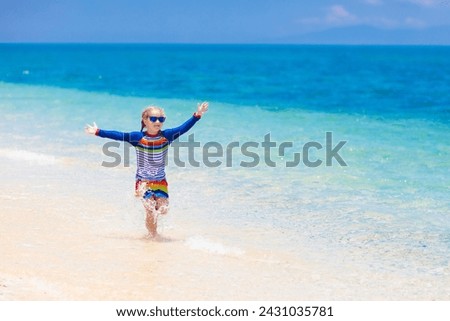 Kids playing on tropical beach. Children swim and play at sea on summer family vacation. Sand and water fun, sun protection for young child. Little girl running and jumping at ocean shore.
