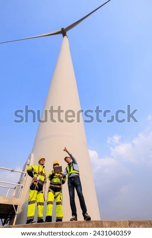 Engineer team hold using tablet standing to talk planing project in the wind turbines farm. renewable energy installation project for the future world concept. wide angle shot
