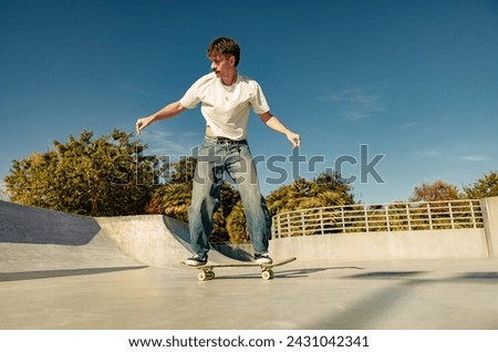 Excited young man riding skateboard in skate park on sunny day. Extreme sport concept Royalty-Free Stock Photo #2431042341