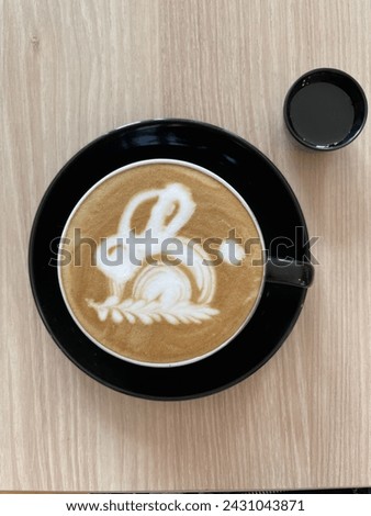 A cup of coffee with foam framing a bunny picture, with small cup for additional brown sugar.