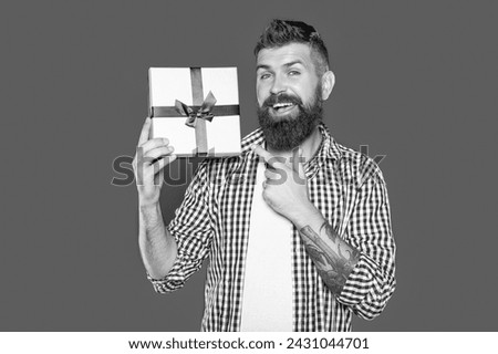 mature bearded guy with present box on grey background. pointing finger