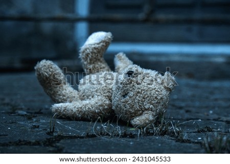 Conceptual image: lost childhood, loneliness, pain and depression. Dirty toy Teddy bear lying down outdoors. Selective focus. Royalty-Free Stock Photo #2431045533