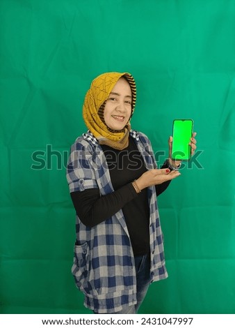 Happy adult asian woman showing green screen on her smartphone. Isolated on green background