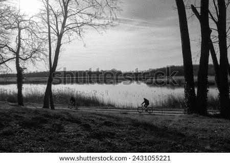 Couple riding bike through park next to lake in sunset. Zobnatica lake, near Backa Topola, Serbia. Black and white photo.
