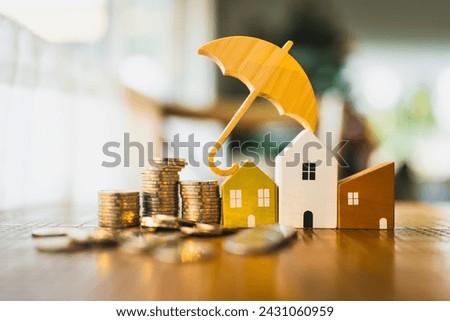 A picture of a house model and a pile of money with a umbrella symbol on top, a concept related to home insurance, house protection and insurance related expenses.