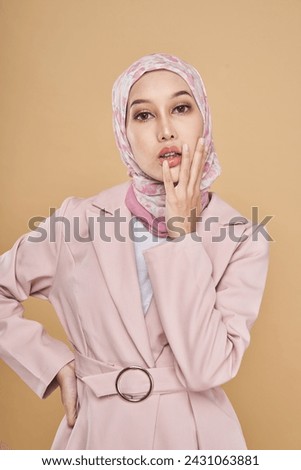 Portrait of a beautiful Muslim female model wearing stylish pink office attire with hijab isolated over beige  studio background. Fashion, beauty, style concept.