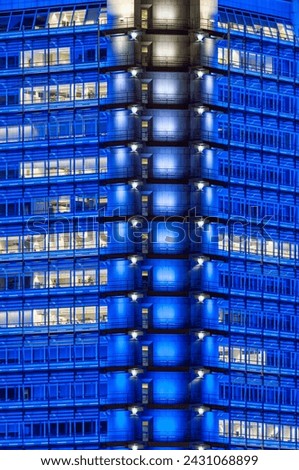 Blue illuminated facade of a high-rise office building at night in the dark with partially illuminated open-plan offices Royalty-Free Stock Photo #2431068899