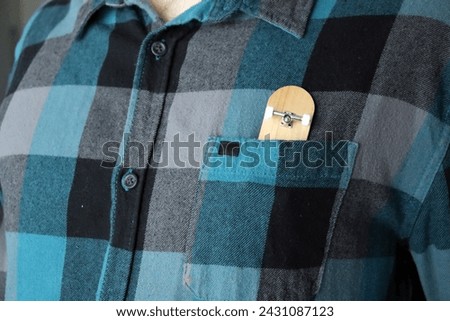 Blank wooden fingerboard in a flannel skate shirt pocket, close up. Mini skateboard, small skateboard deck