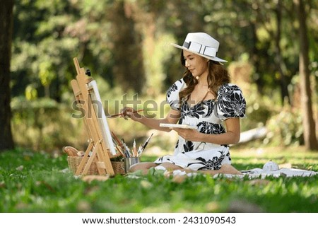 Beautiful young woman in casual dressed painting a picture on a canvas during a picnic in the park