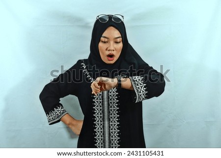 beautiful young Asian Muslim woman wearing hijab and black dress with white pattern raised his arm and looking wristwatch. put glasses on her head isolated on white background