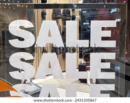 Close-up of a 'SALE' sign on a shop window with reflections of the street and storefronts.
