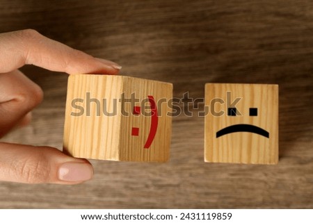 Woman choosing cube with happy face instead of another one with sad at wooden table, top view