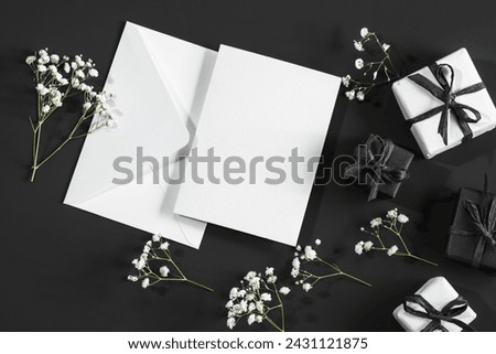 White and black gift boxes on a black background and a white envelope and sprigs of gypsophila.