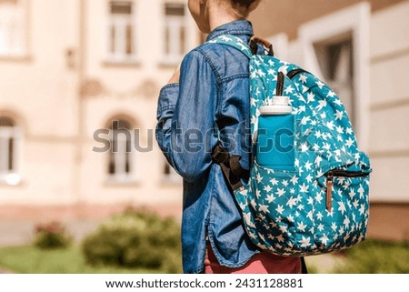 Reusable Water Bottle in School Backpack in Child Schoolgirl on School Background. Modern Blue Collapsible Silicone Bottle in Bag Royalty-Free Stock Photo #2431128881