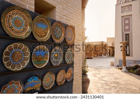 Traditional ceramic and copper plate with ornament at souvenir stall in Samarkand Eternal city Boqiy Shahar Registan complex at sunset near river in Uzbekistan.  Royalty-Free Stock Photo #2431130401